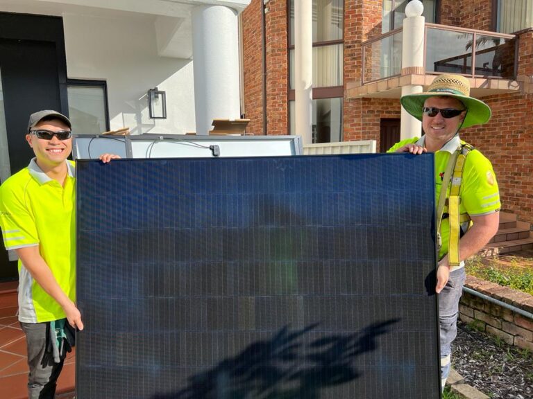 Two technicians holding large solar panel indoors